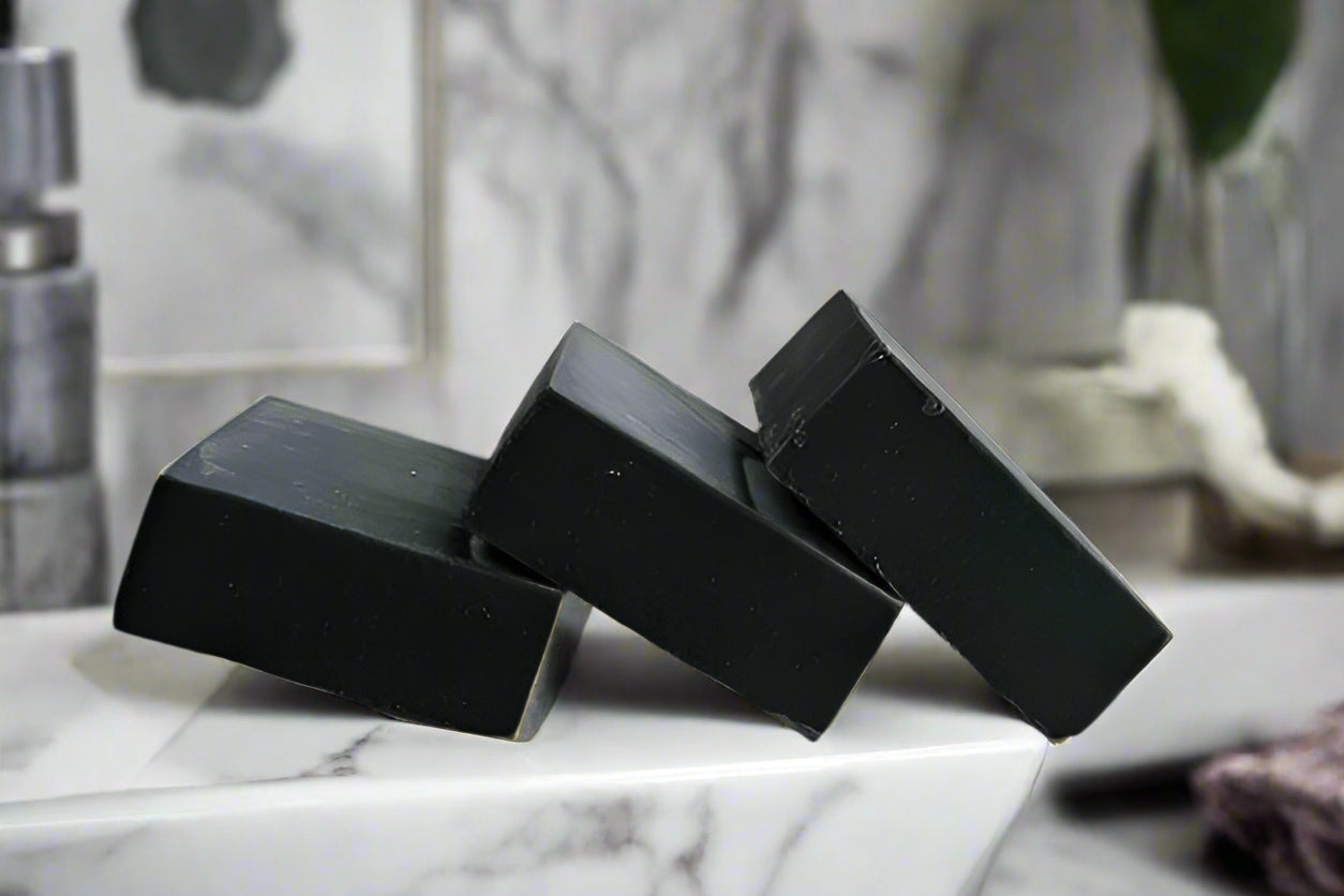 Three bars of unscented activated charcoal soap placed on a white plate against a white background.