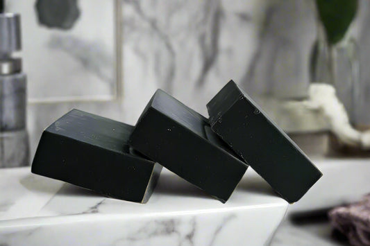 Three bars of unscented activated charcoal soap placed on a white plate against a white background.